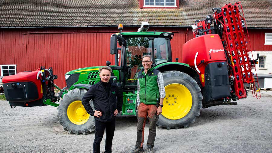 to menn i arbeidsantrekk står foran en grønn traktor og en rød låve