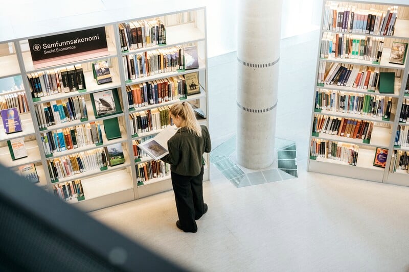 bilde av en dame som står å leser en bok foran en bokhylle